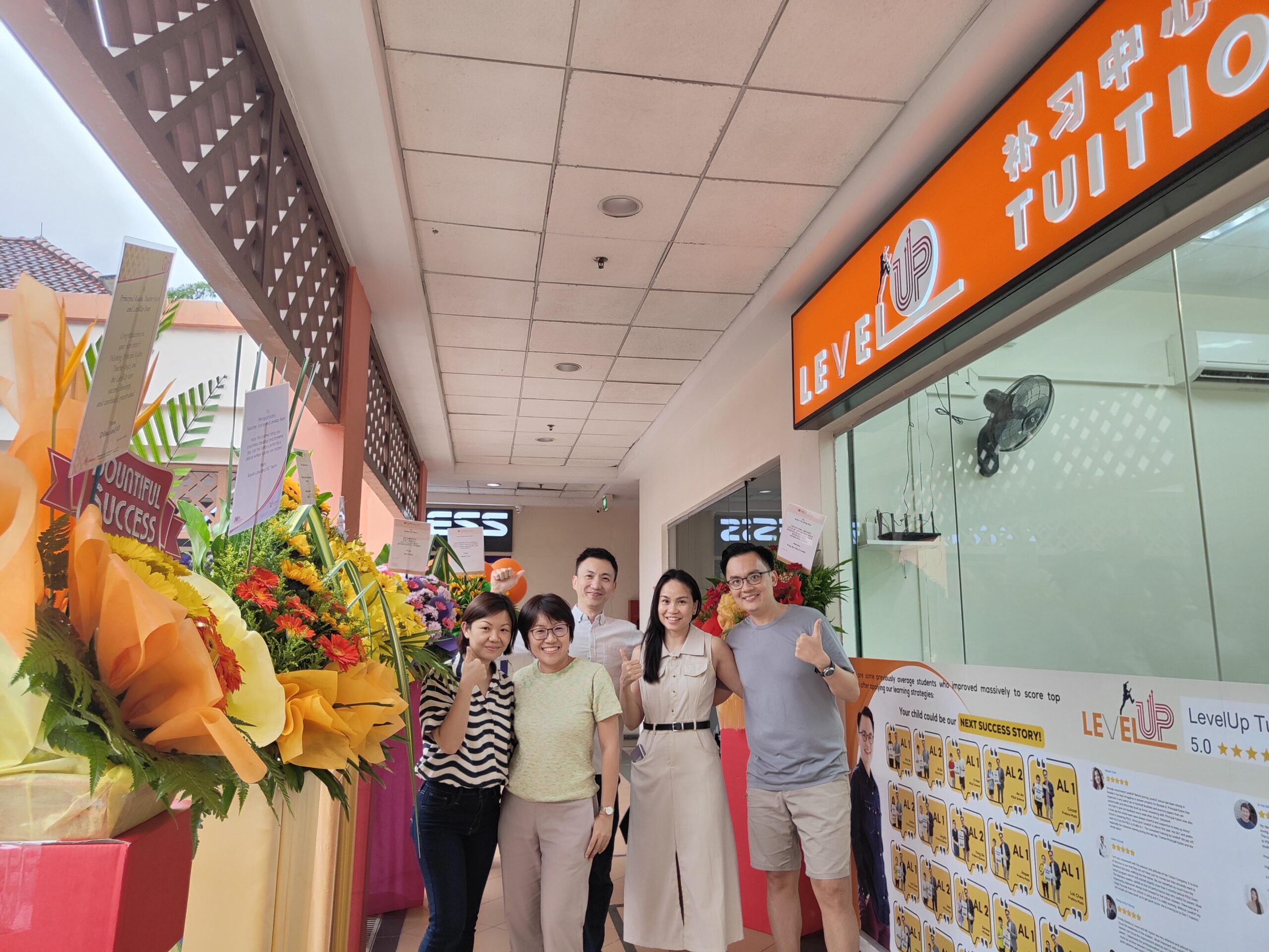 LevelUp Tuition team celebrating the grand opening of their Hougang branch, standing in front of the tuition center with congratulatory flower stands.
